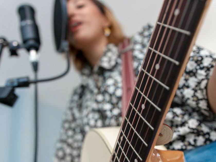 Sängerin mit Akustikgitarre singt vor einem Studiomikrofon
