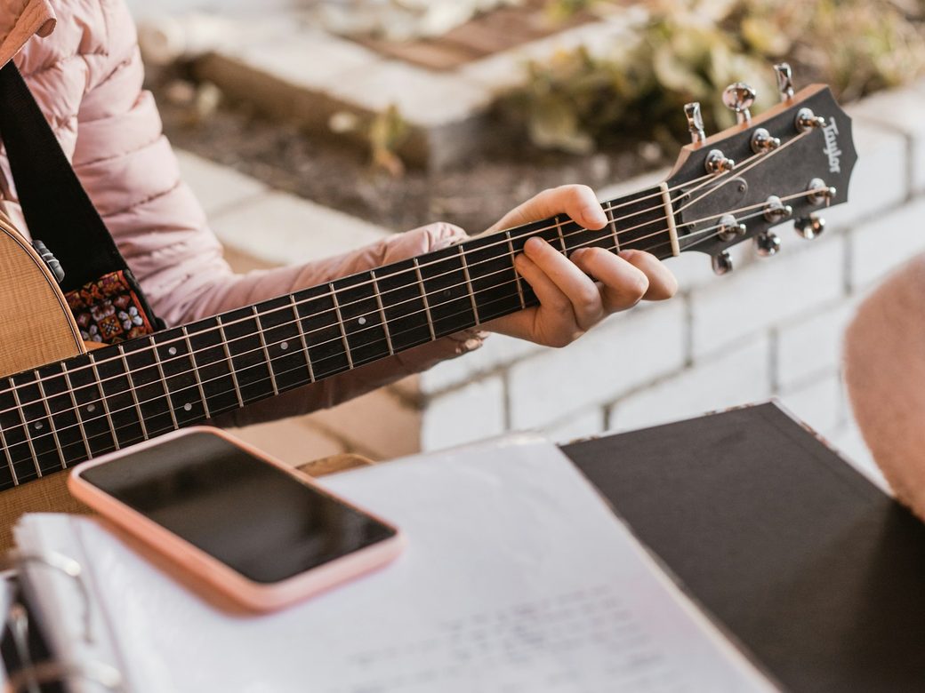 Hände auf einer Akustikgitarre neben einem handgeschriebenen Notenblatt